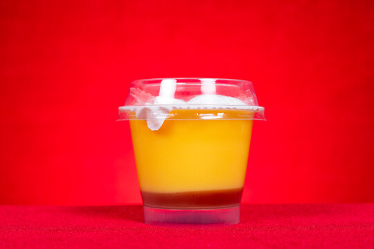 Caramel pudding in transparent plastic cup against red fabric background