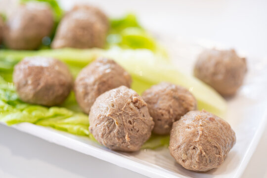 Beef meatballs laid on fresh lettuce on a white rectangular plate