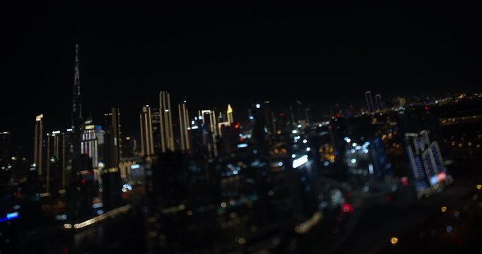 Timelapse of the Dubai skyline at night with soft bokeh lights and the blurred silhouette of Burj Khalifa standing tall against the dark sky