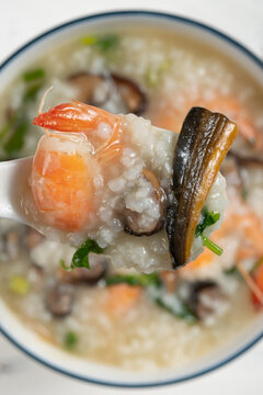 Spoonful of seafood congee with shrimp, eel and mushrooms above a ceramic bowl