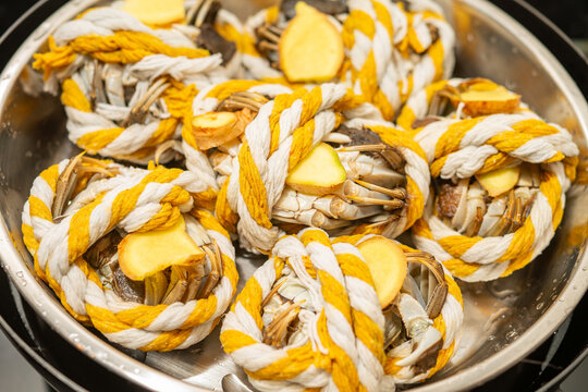Hairy crabs bound with striped rope and ginger slices placed inside stainless steel steamer pot