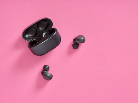 Wireless earbuds with charging case on pink background