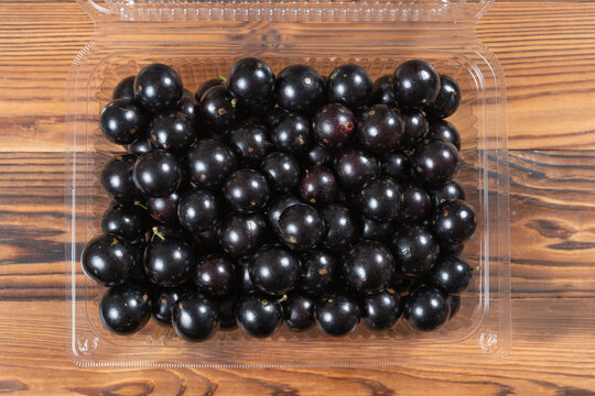 Fresh jabuticaba fruits densely packed inside a transparent plastic clamshell container on wooden planks