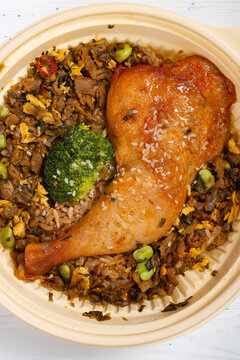 Roasted chicken leg over mixed vegetable fried rice served in disposable lunch bowl