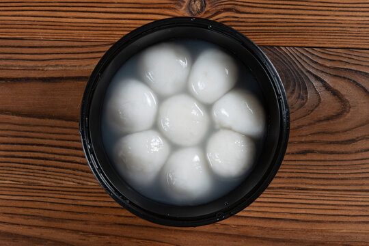 Glutinous rice tangyuan soaking in clear water inside a black plastic bowl on wooden planks