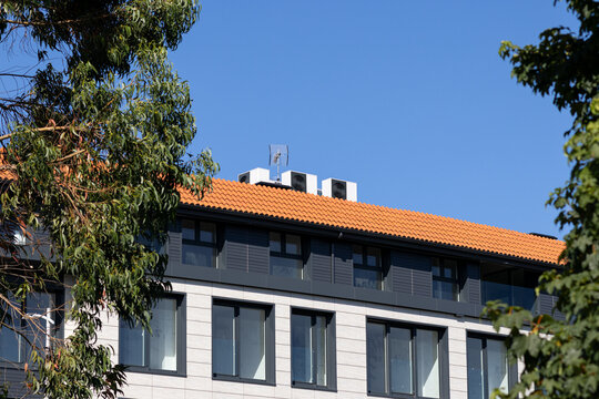 modern building exterior with red tile roof and air conditioning units framed by trees