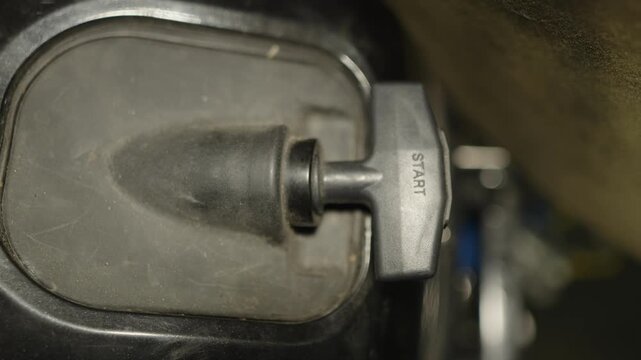 A top-down shot of a black plastic manual pull start handle with a "START" inscription on an outboard boat motor.
