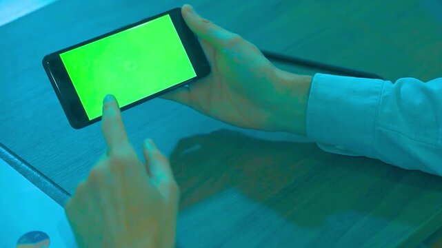 Person using mobile phone with green screen mockup in blue lighting