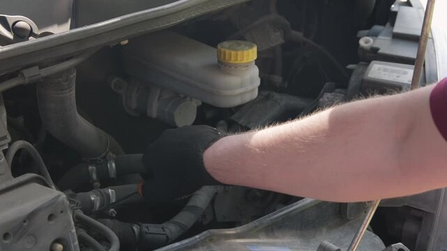 Close-up of a mechanic using a screwdriver to remove a part under the hood of a car