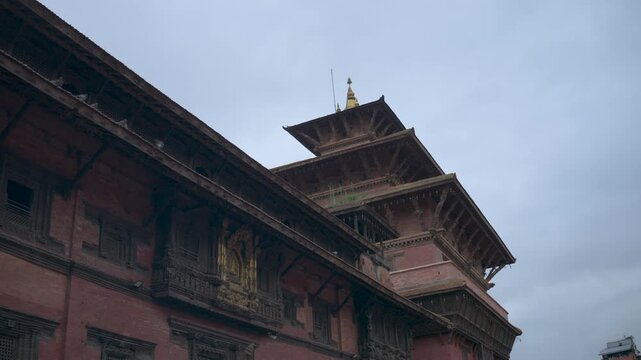 Low angle perspective looking up at the ornate carved wooden windows and tiered roof of a traditional Newari palace in Lalitpur