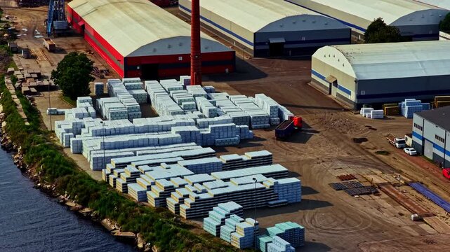 Riga, Latvia - 26 August 2025: Aerial view of industrial port area with large stacks of construction materials, warehouses, and riverfront.