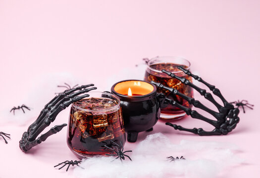 Halloween spooky drinks with ice in glasses, black skeleton hands, fake spiders and candle.