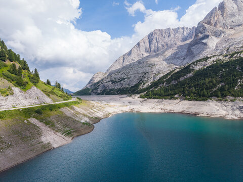 Aerial view of Fedaia Lake with low water levels and exposed shorelines surrounded by the Marmolada glacier and the Dolomites mountain range in Italy.