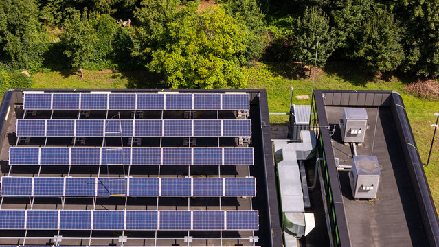 Aerial view of solar panels installed on a flat roof with HVAC equipment and surrounding green trees in Gdansk, Poland.