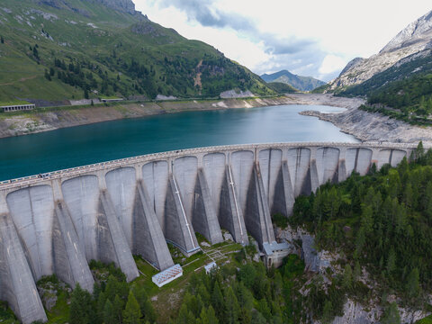 Aerial view of Fedaia Dam and the reservoir in the Dolomites, featuring the concrete structure, surrounding mountain landscape, and exposed shoreline of the lake in ITALY.