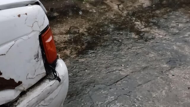 rain falling on the concrete and near the car, accompanied by the sound of rain and thunder