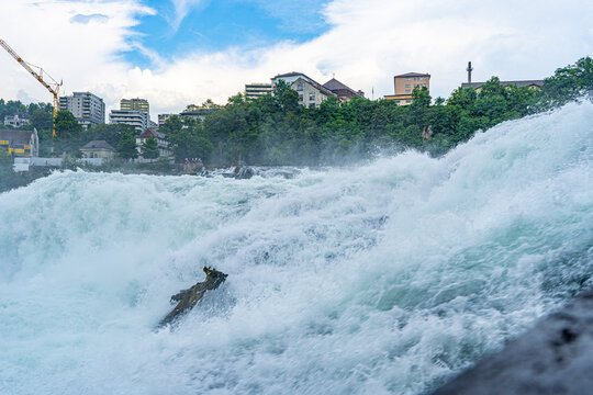 Rhine Falls Waterfall in Switzerland with Foaming Water, City Buildings, and Blue Sky.