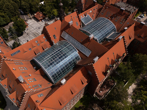 Aerial view of the Gdansk University of Technology, featuring its distinctive red-tiled roofs, large glass atrium, and historic brick architecture in Gdansk, Poland.