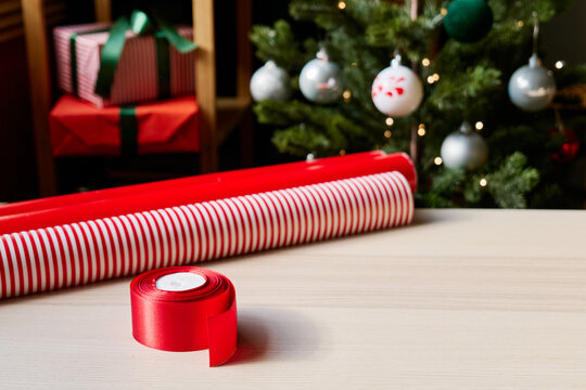 Christmas gifts preparation table with wrapping paper, gift, ribbon and xmas balls. Festive mood.