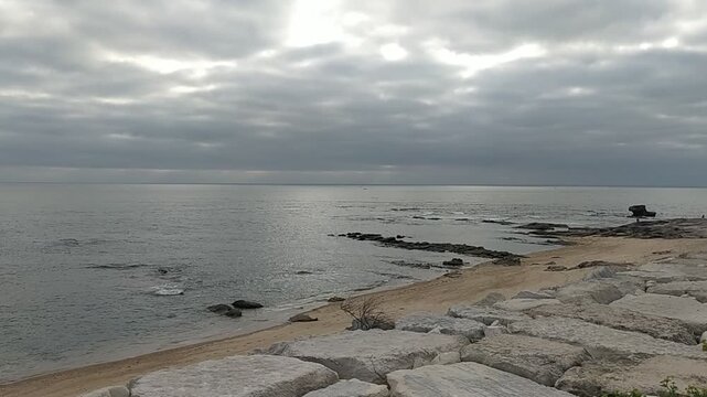 A calm, melancholic seascape featuring rocky shores and a gray, overcast sky. This serene coastal landscape with no people evokes solitude, perfect for themes of nature, reflection, and peace.