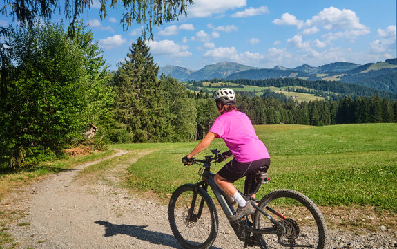 Active senior woman riding an e-mountain bike on a scenic alpine trail beneath the Nagelfluh mountain range on a sunny summer day. Oberstaufen, Allg&auml;u, Bavaria, Germany.