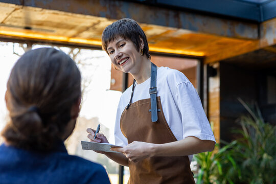Woman in the apron in a cafe getting an order from the male customer