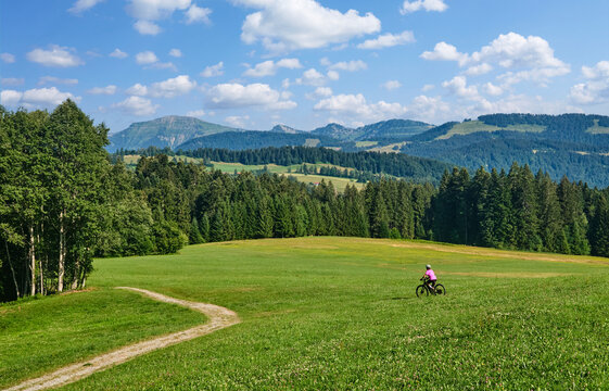 Active senior woman riding an e-mountain bike on a scenic alpine trail beneath the Nagelfluh mountain range on a sunny summer day. Oberstaufen, Allg&auml;u, Bavaria, Germany.