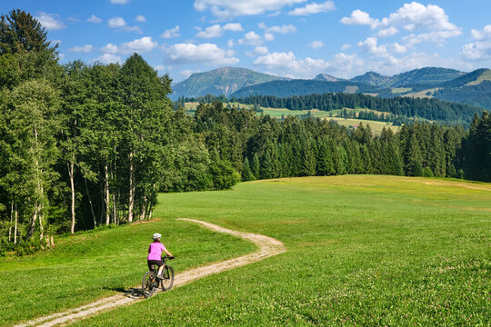 Active senior woman riding an e-mountain bike on a scenic alpine trail beneath the Nagelfluh mountain range on a sunny summer day. Oberstaufen, Allg&auml;u, Bavaria, Germany.