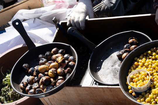 Street food stall in South Korea with roasted chestnuts (Castanea) in black pans and a container of yellow berries.