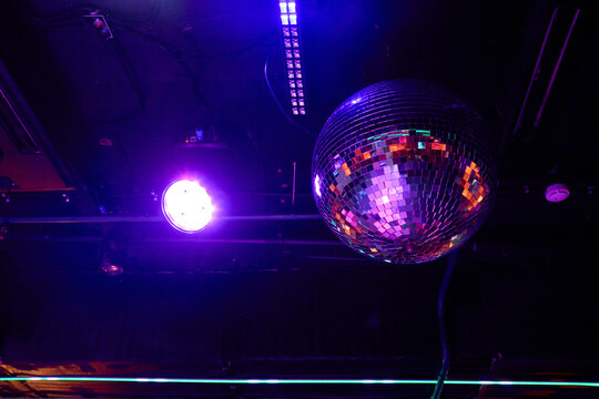 Shiny spherical mirror ball reflecting vibrant purple white club lights on dark event venue ceiling, creating energetic festive nightlife party atmosphere for dancing music entertainment celebration