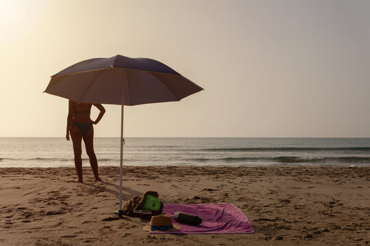 Beach umbrella with towel backpack book hat and woman by the sea
