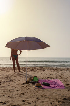 Vertical beach umbrella with towel backpack and woman by sea