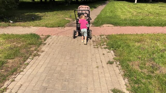 Little girl pushing her toy stroller outdoors, pretend parenting play and childhood development activity in a park