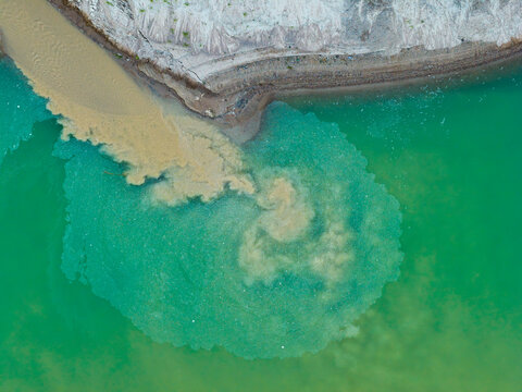 Aerial view of a sand and gravel mine with sediment-rich water flowing into a vibrant green quarry pond, showcasing industrial extraction patterns in Poland.