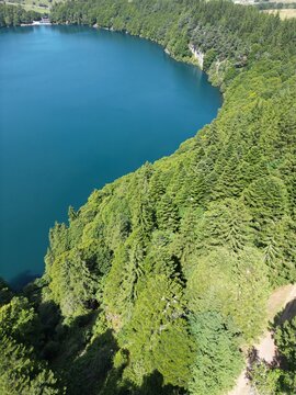 Aerial view of the deep blue waters of Lac Pavin surrounded by dense coniferous forests and steep volcanic crater slopes in Besse-et-Saint-Anastaise, Auvergne-Rhone-Alpes, France.