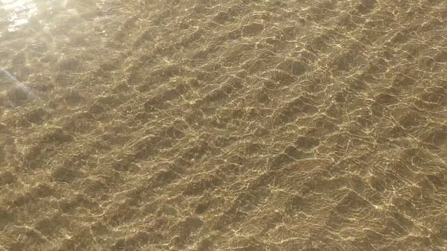 Clear, sundrenched water ripples over a textured sandy seabed, creating a serene, meditative atmosphere. This peaceful, nobody scene evokes tranquility, perfect for nature and wellness themes.