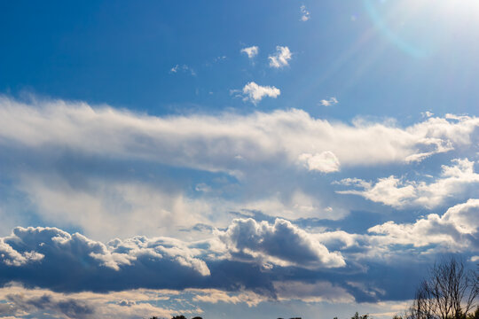Vibrant blue sky with layered, fluffy cumulus and stratocumulus clouds, bathed in bright sunlight. A wide-angle view of nature's beauty and atmospheric drama