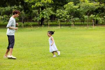 Fototapeta premium child runs with father in summer field, small child playing on the lawn. spending time with father in the park. Happy Asian family having fun time on picnic at city nature park, outdoor activitie