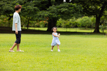 Fototapeta premium child runs with father in summer field, small child playing on the lawn. spending time with father in the park. Happy Asian family having fun time on picnic at city nature park, outdoor activitie