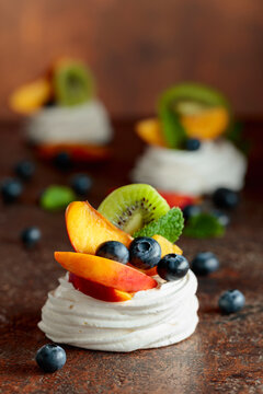 Pavlova dessert with nectarines, kiwis, blueberries, and mint on a vintage background.