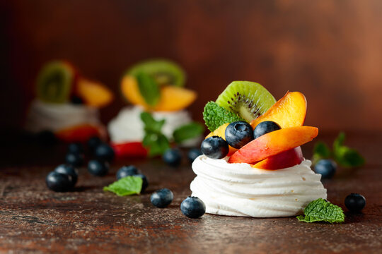 Pavlova dessert with nectarines, kiwis, blueberries, and mint on a vintage background.