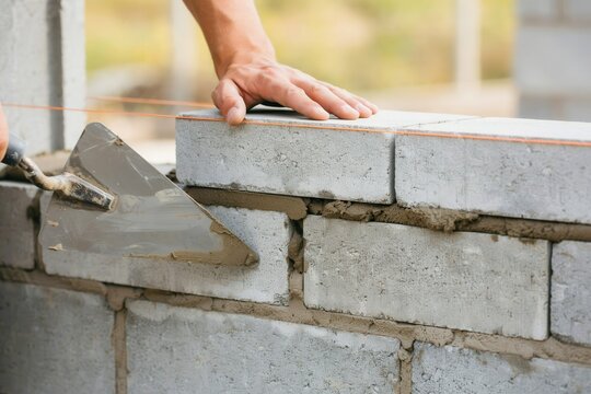 Mason laying concrete block with trowel. Construction site masonry work.