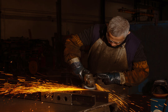 Industrial worker grinding metal with electric grinder and sparks in dark workshop