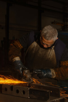 Industrial worker grinding metal with electric grinder and sparks in dark workshop