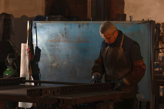 Industrial worker preparing metal pieces for welding in workshop