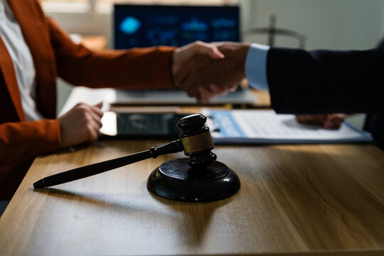 Lawyer and client shaking hands after successful legal settlement with judge gavel on desk.