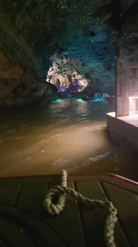 Tourists traveling by boat through a dark cave with glowing lights on the ceiling. Underground river adventure exploring natural geological formations in a grotto.
