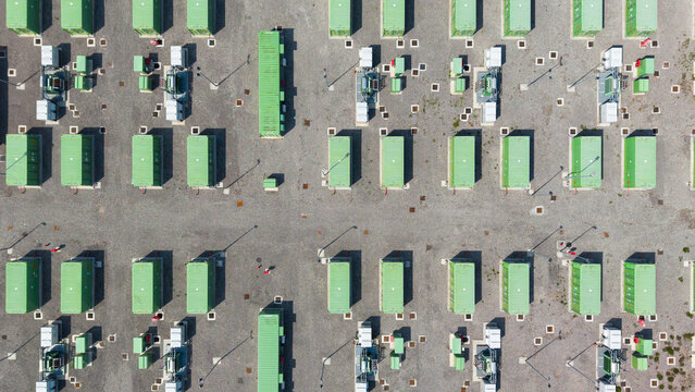 Aerial view of a Battery Energy Storage System BESS facility with rows of green storage containers and electrical equipment on a gravel site in Tavazzano con Villavesco, Lombardy, Italy.