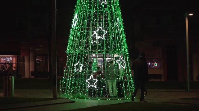 People walking by green christmas tree lights at night in bilbao city park