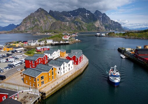 Colorful houses hug the fjord, boats glide on calm waters, and towering peaks rise behind&mdash;Henningv&aelig;r&rsquo;s harbor glows with Nordic charm, a vivid blend of nature and village life